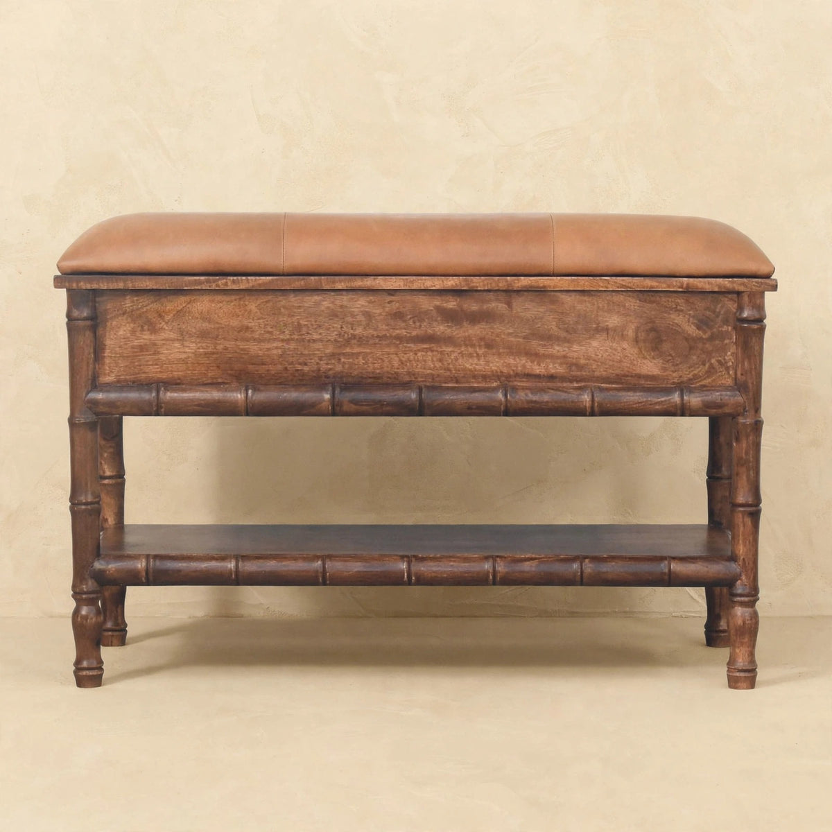 Close view of the carved front of a mango wood bench with a mocha leather cushion in a home interior