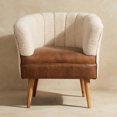 Front view of a cream boucle armchair with a buffalo hide leather seat and wooden legs