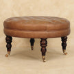 Brown tufted leather round ottoman used as a footrest beside a sofa