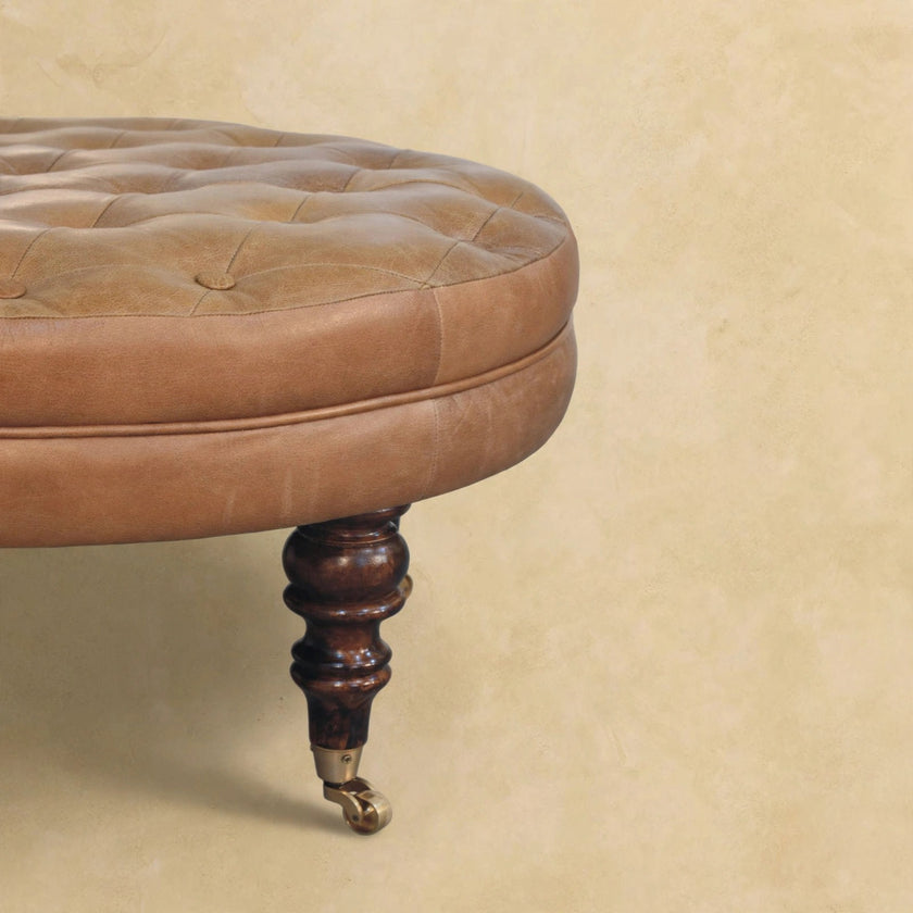 Round buffalo leather ottoman with walnut-finish mango wood legs styled in a room