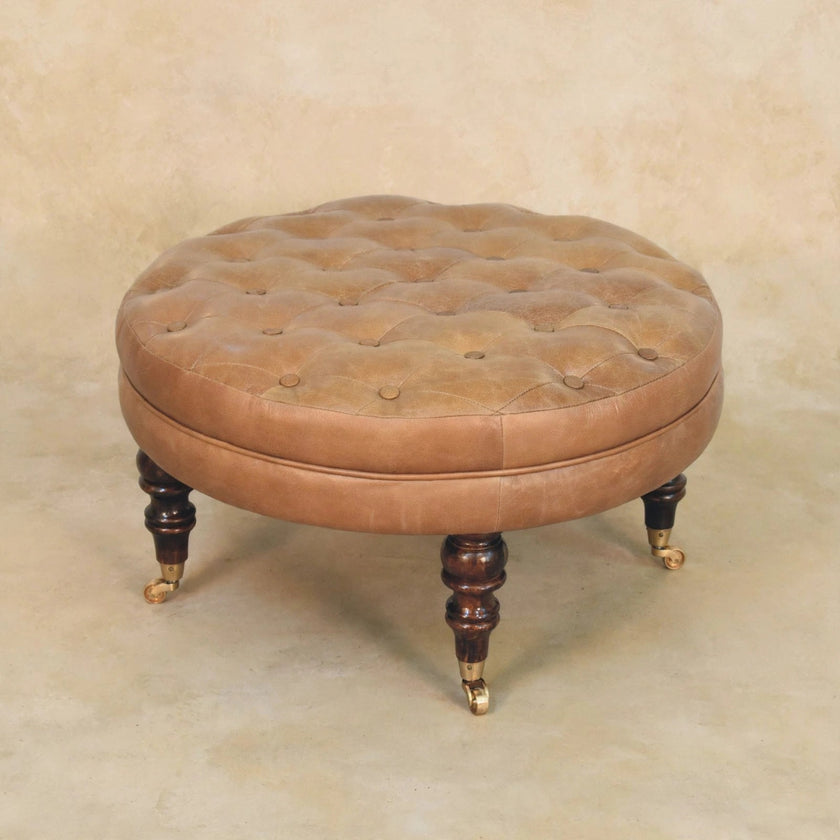 Side view of brown leather round ottoman with turned legs and brass casters