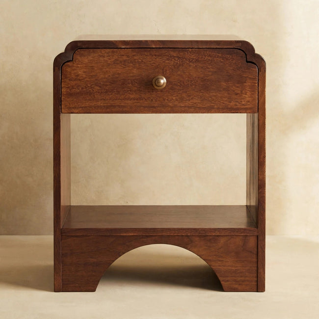 Walnut-finish mango wood bedside table with drawer and brass knob beside a bed