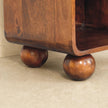 Bedside table with woven front and one drawer next to a bed with a lamp