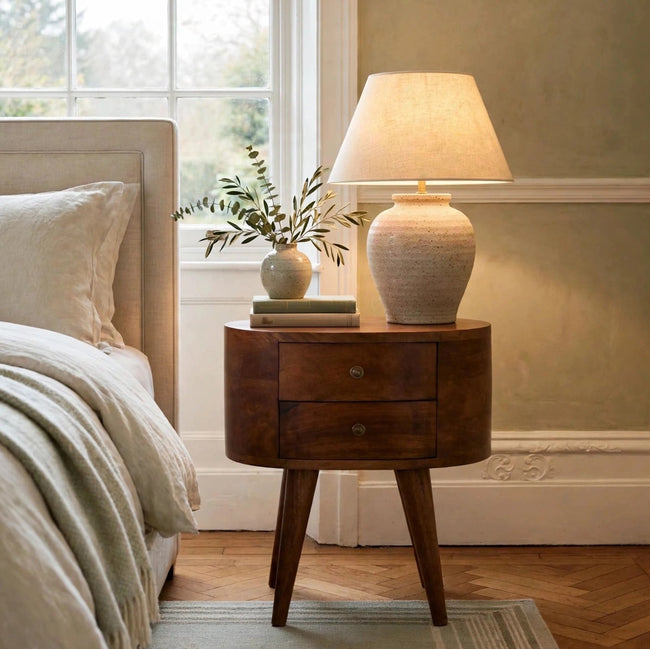 Chestnut rounded bedside table in solid mango wood shown in a bedroom setting