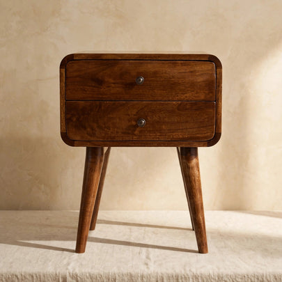 Chestnut mango wood bedside table with two drawers and shiny knobs beside a bed