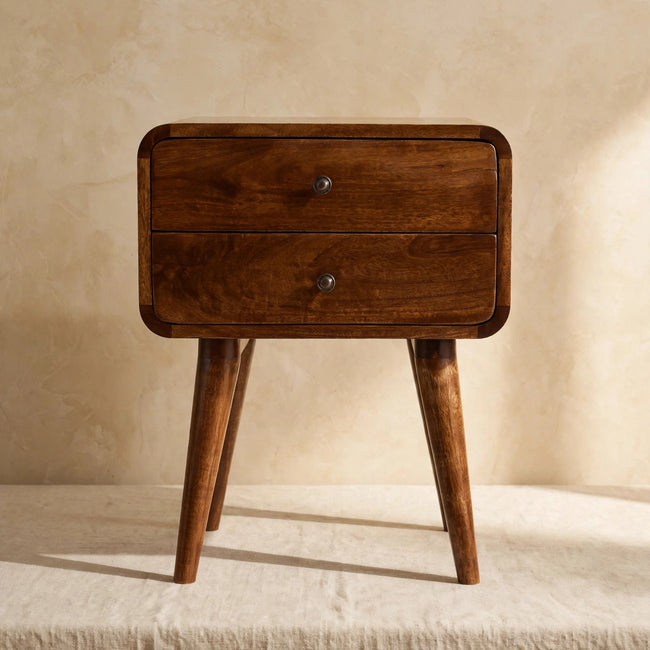 Chestnut mango wood bedside table with two drawers and shiny knobs beside a bed