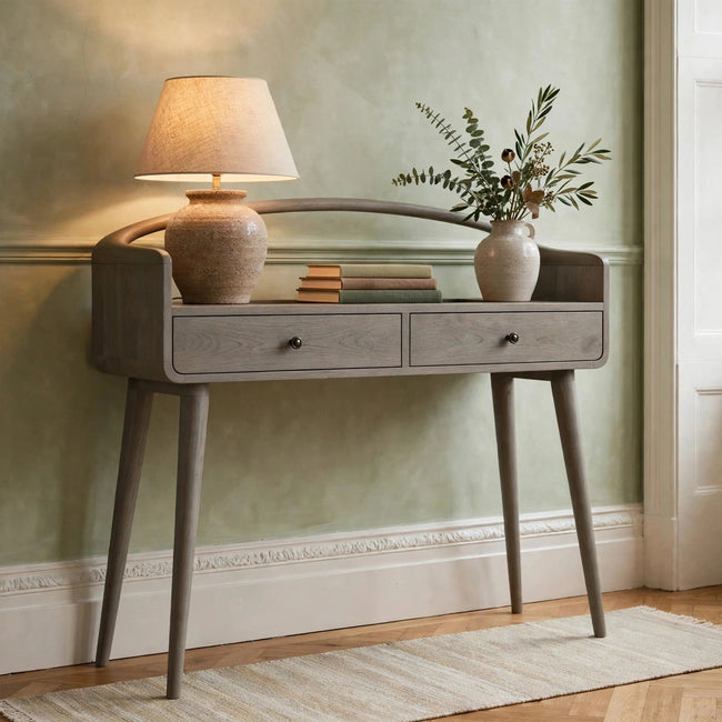 Curved grey-wash solid mango wood console table with two drawers, shown in a room setting