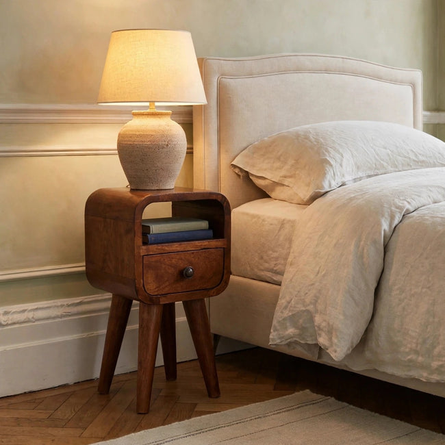 Small chestnut mango wood bedside table with curved edges in a bedroom setting