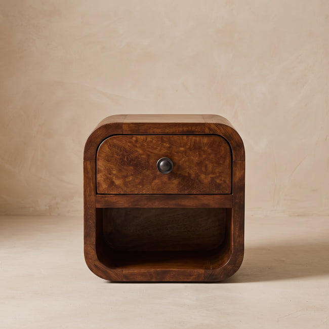 Small solid mango wood bedside table with curved edges beside a bed
