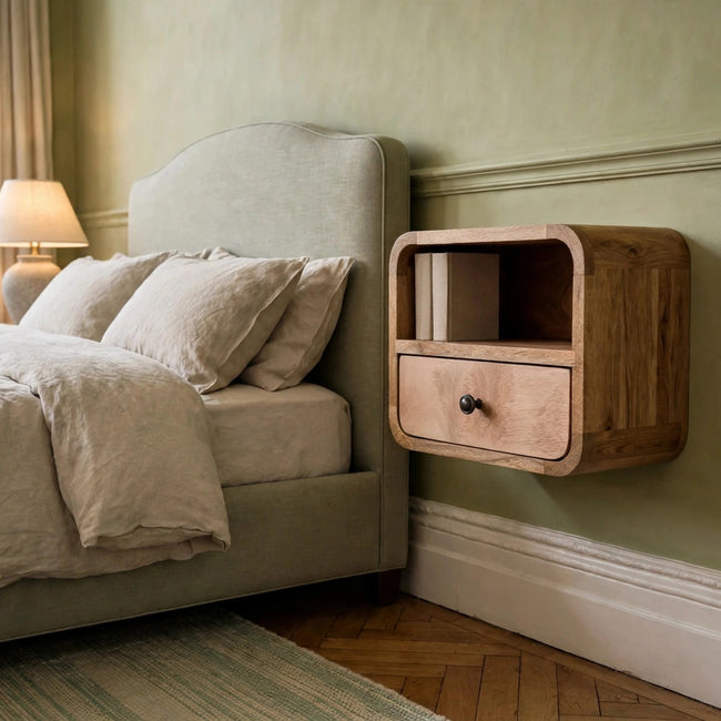 Small curved wall mounted bedside table in an oak-ish finish with a drawer and open shelf, shown in a bedroom
