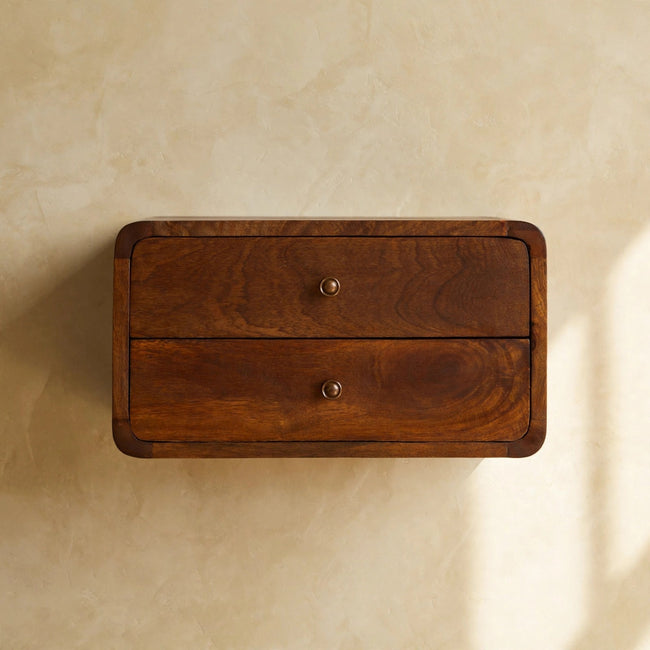 Wall-mounted chestnut bedside table with two drawers and shiny knobs beside a bed