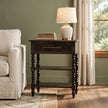 Carbon ash solid mango wood side table with turned legs, one drawer and two open shelves in a living room