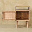 Angled view of the mango wood bedside table showing its rattan door and legs