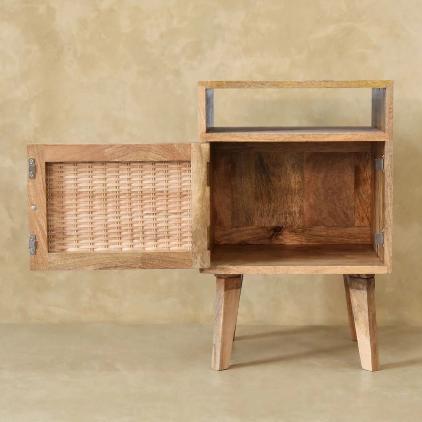 Angled view of the mango wood bedside table showing its rattan door and legs