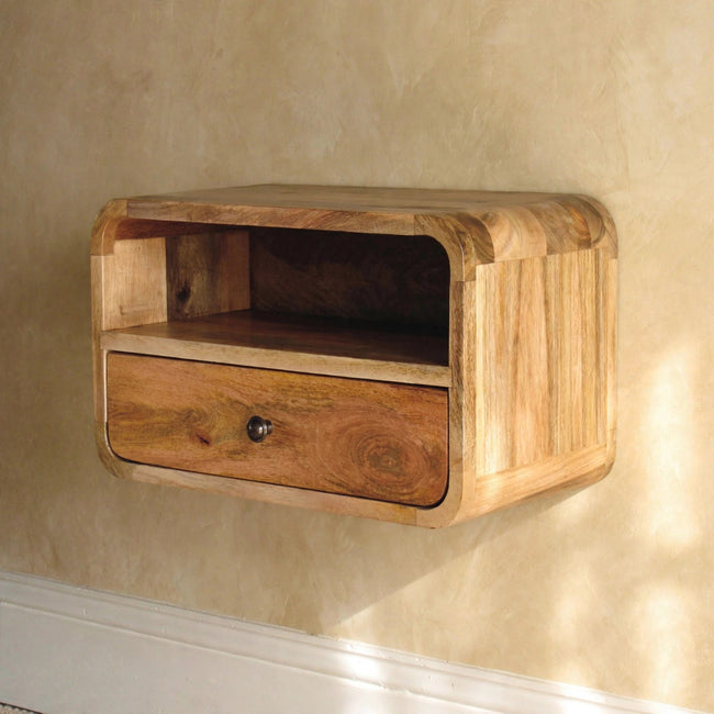 Wall-mounted solid mango wood bedside table with a curved edge beside a bed