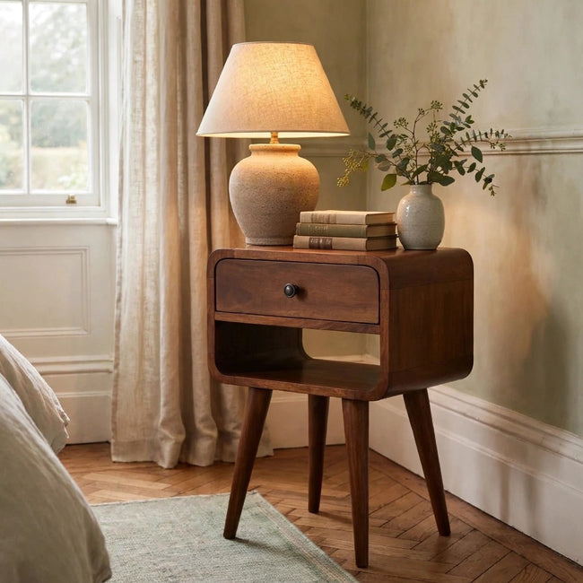 Small chestnut solid mango wood bedside table with curved edges in a bedroom