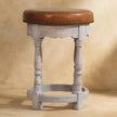 Brown leather seat with antique brass studs on the mango wood frame of the Rustic Charm stool