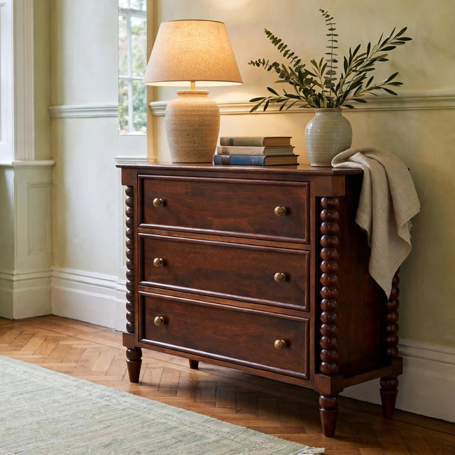 Spindle Winewood Chest, a three-drawer mango wood chest with brass knobs, shown in a room setting